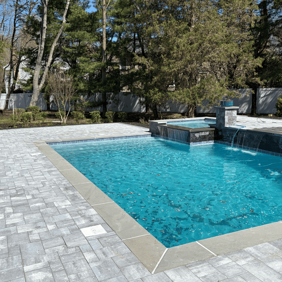 Pool with stone deck and water fountain in backyard landscape.