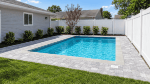 Backyard swimming pool with white fence and lush greenery.