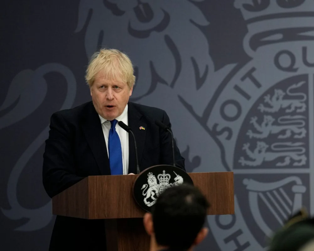 Boris Johnson speaking at a press conference with UK emblem in background.