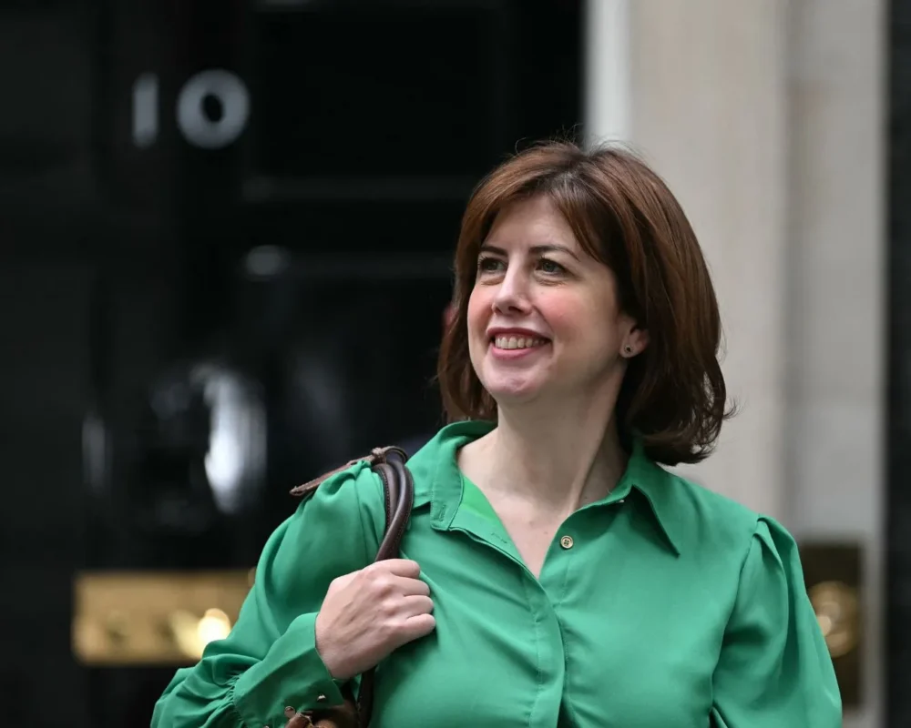 Woman smiling outdoors in green shirt, holding a bag.