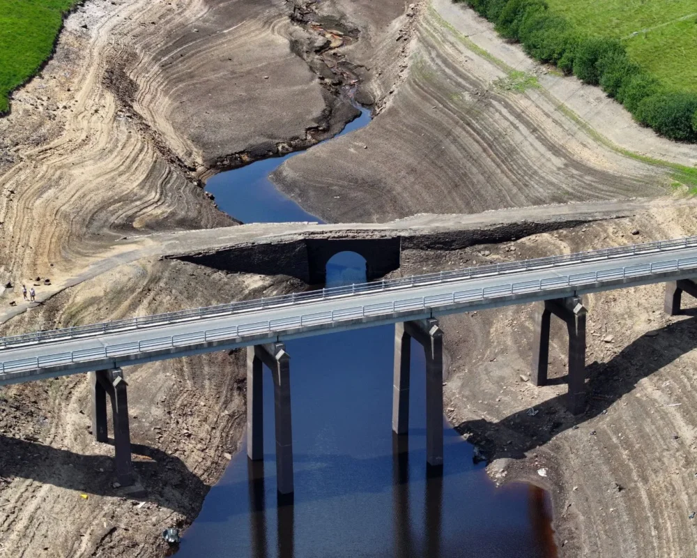 Drought-affected reservoir with bridge and exposed land.