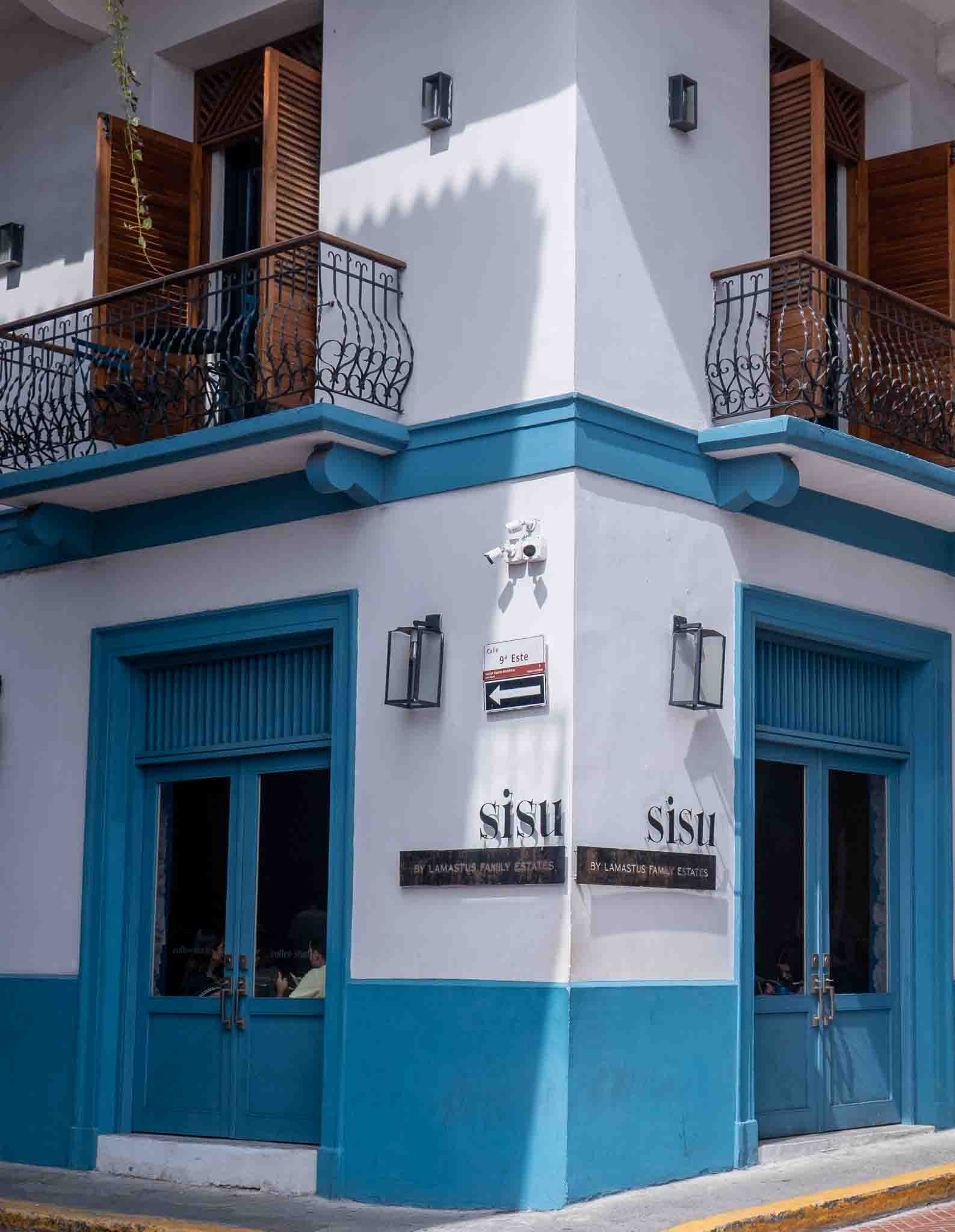 Exterior corner of Sisu in Casco Viejo with white walls, bright blue trim, wood shutters, and black iron balconies