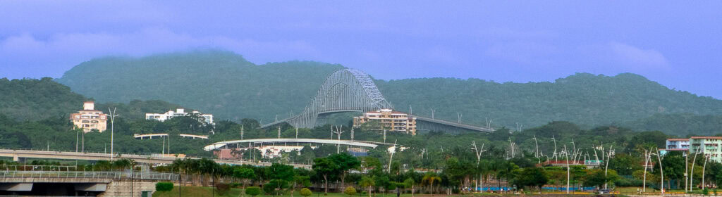 Panoramic view of the Bridge of the Americas spanning the Panama Canal, surrounded by tropical hills and urban buildings.