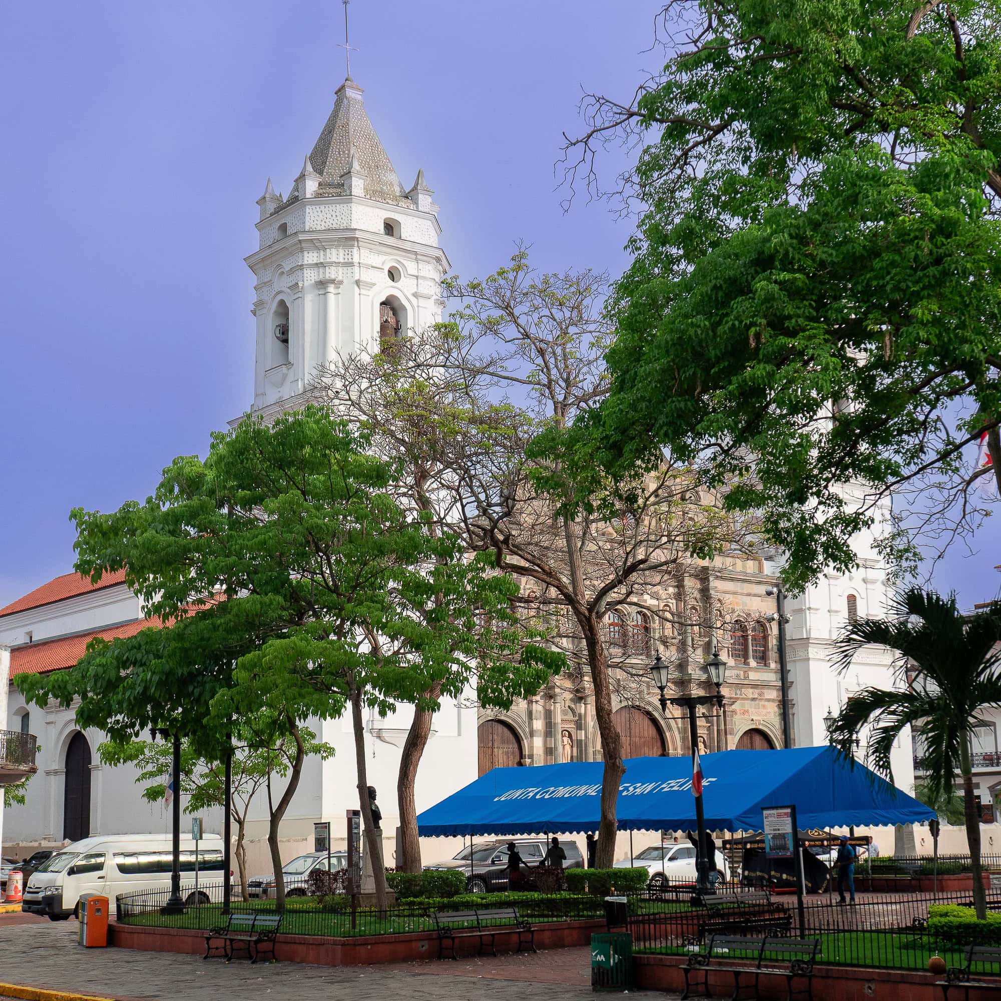 Metropolitan Cathedral and Plaza Catedral in Casco Viejo, Panama, with park benches, lush trees, and local artisan stalls under blue awnings.