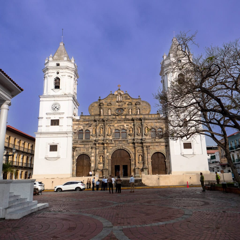 Front view of the Metropolitan Cathedral in Casco Viejo, Panama, with twin white towers, a stone façade, and visitors gathered in the plaza.