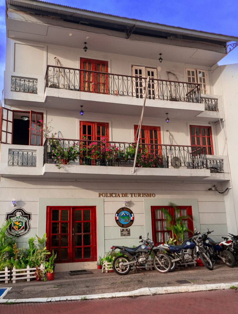 Tourist police station in Casco Viejo, Panama, with red balconies, potted plants, and parked motorcycles