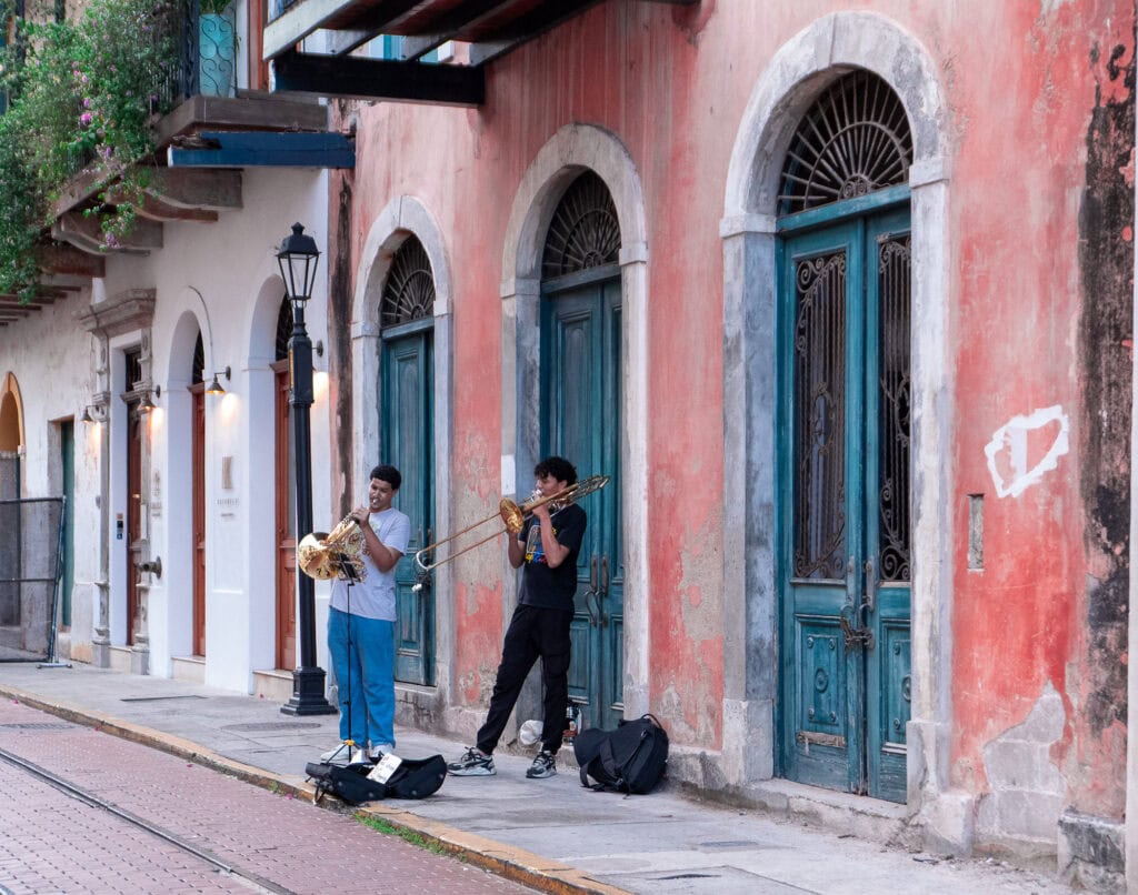Two street musicians playing brass instruments in front of a colorful building in Casco Viejo, Panama.