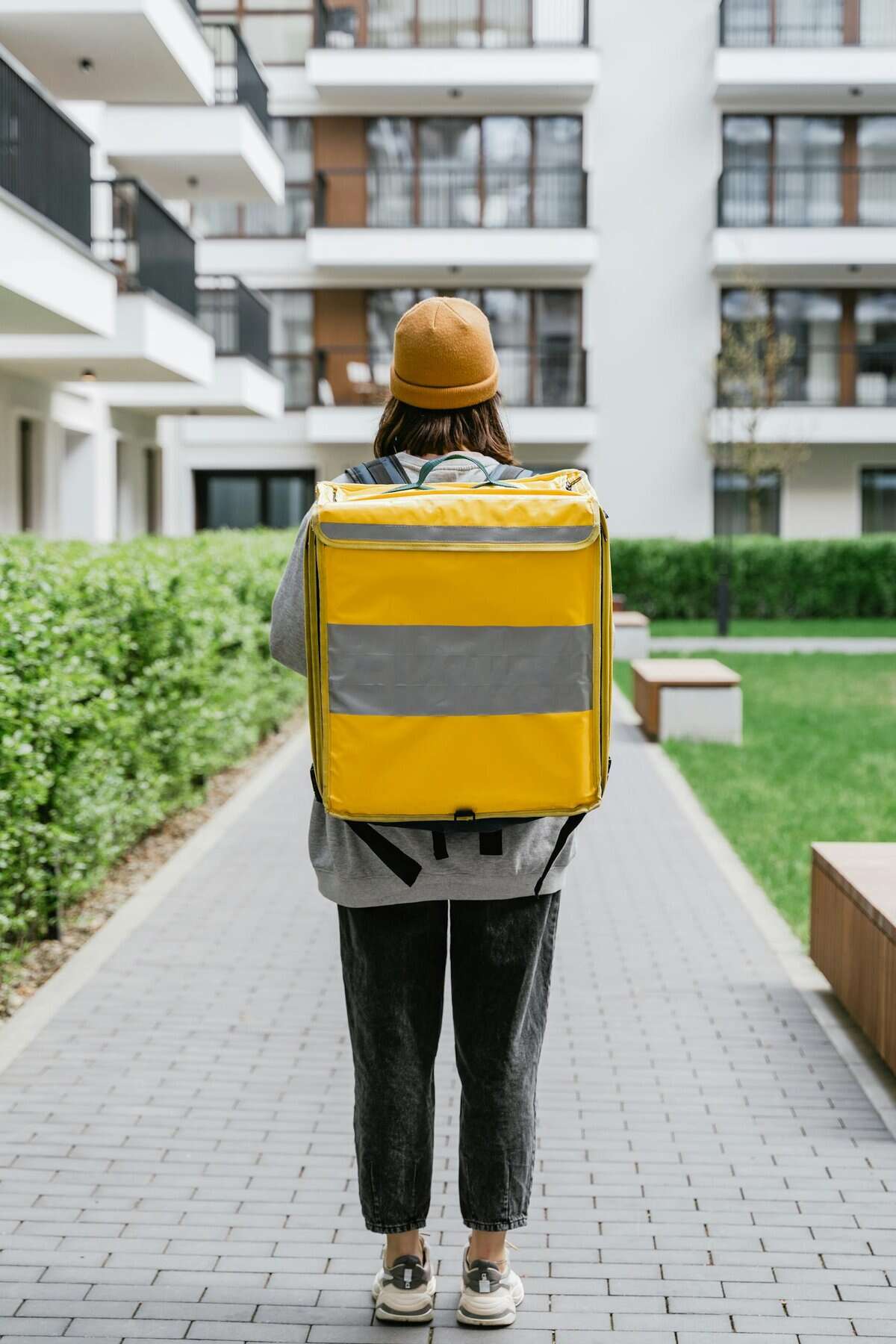 Rear view of a delivery person with a yellow thermal bag in an urban setting. Perfect for logistics themes.