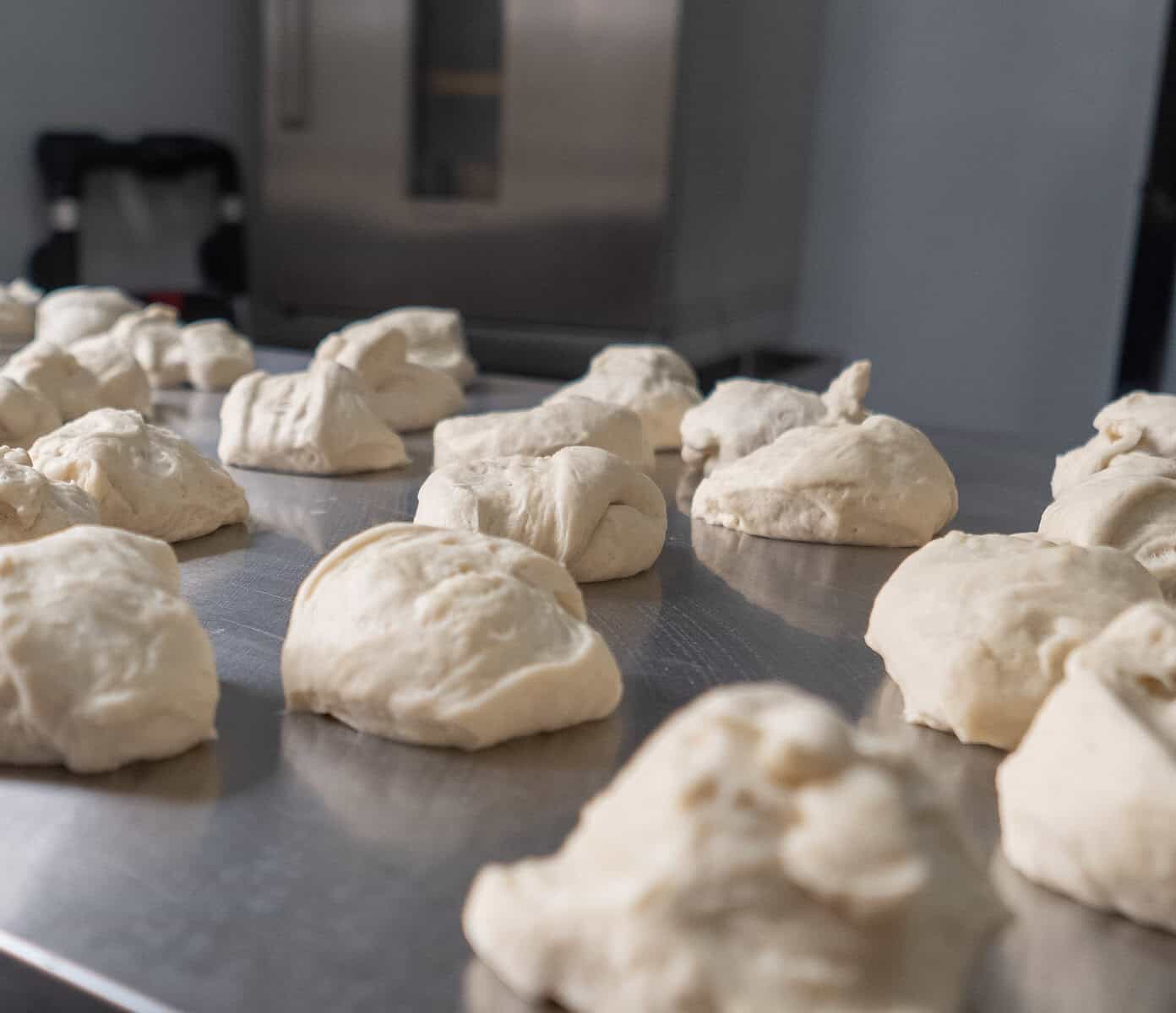 Small portions of raw dough resting on a stainless-steel table before shaping.