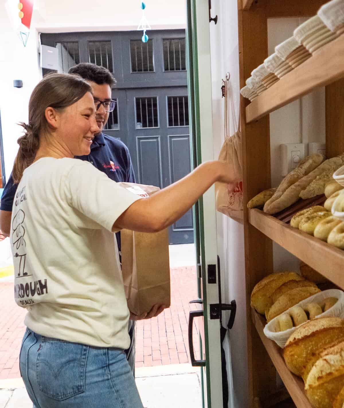 Caroline handing a pre-order bag of fresh sourdough to a customer inside her small Casco Viejo bakery space.
