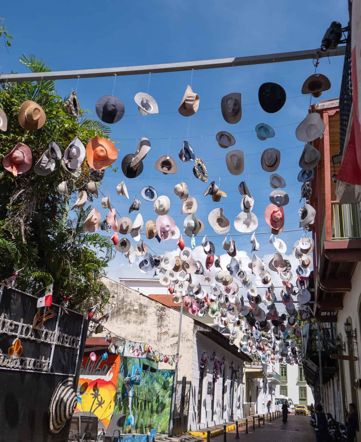 Colorful Panama hats hanging above a narrow street in Casco Viejo, Panama City, creating a vibrant canopy against a bright blue sky.