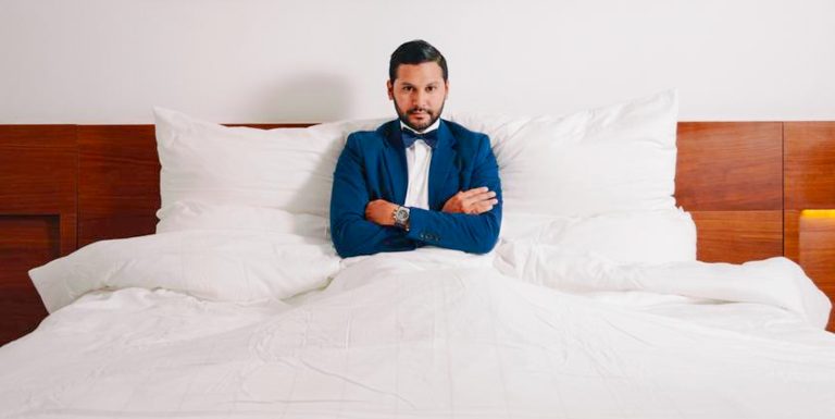 Hotel guest experience moment with well-dressed man seated on bed, representing high standards and attention to detail in hospitality