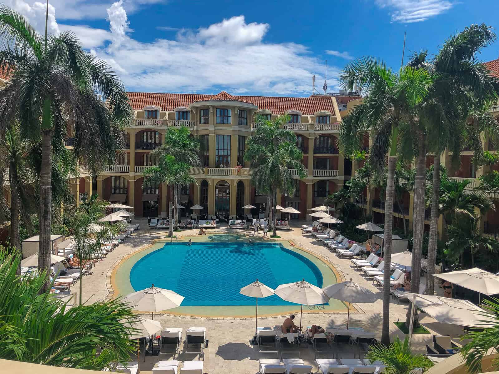 Palm-lined courtyard pool at Sofitel Legend Santa Clara Cartagena beneath a bright blue sky.