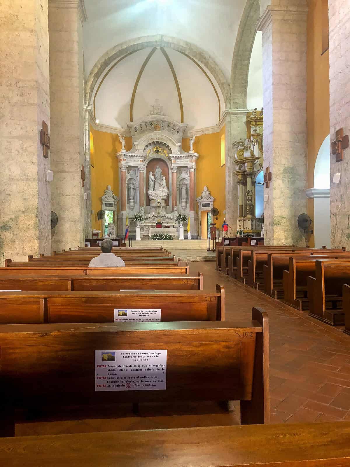 Interior of Santo Domingo Church in Cartagena with wooden pews, stone columns, vaulted ceilings, and an ornate altar.