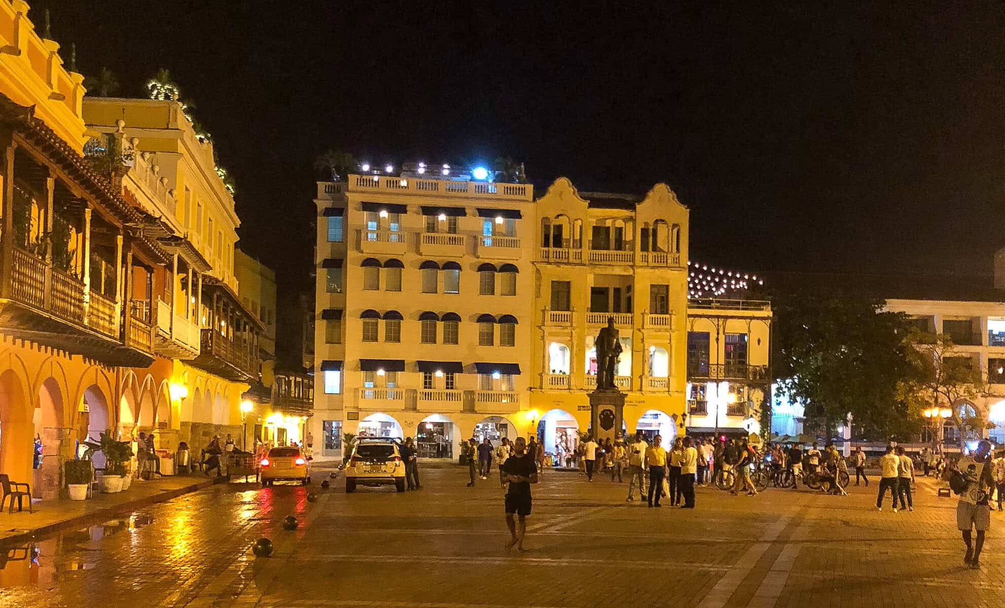 Visitors gathering in Cartagena’s illuminated Plaza de la Aduana surrounded by historic colonial buildings at night.