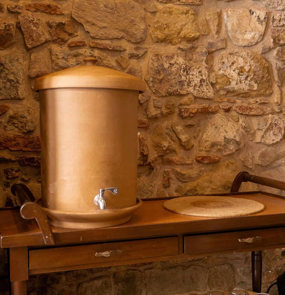 Terracotta coloured water dispenser on a wooden sideboard against an exposed stone wall inside The Vegan Shack in Casco Viejo.