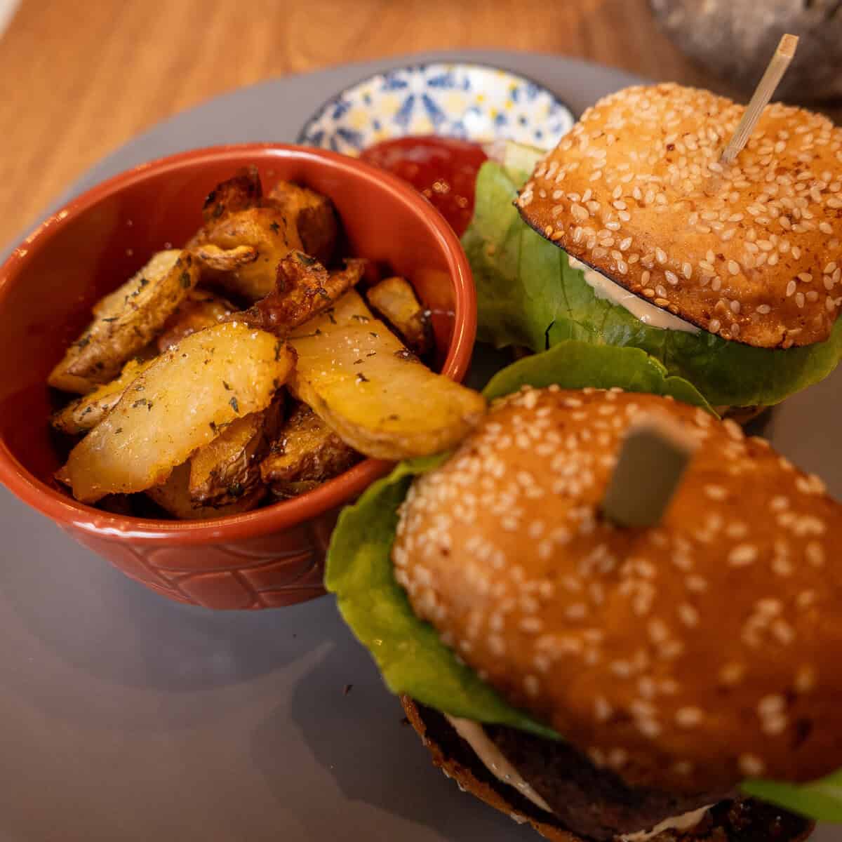 Two vegan burgers with sesame buns, fresh lettuce, dipping sauce, and roasted potato wedges at Vegan Shack in Casco Viejo, Panama.