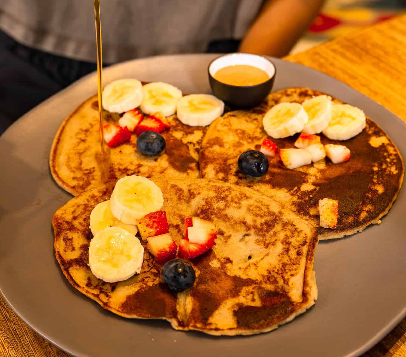 Vegan banana pancakes topped with sliced banana, strawberries, blueberries, and syrup at Vegan Shack in Casco Viejo, Panama.
