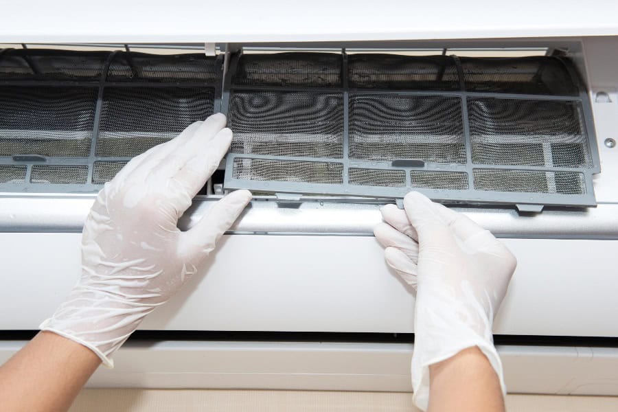Person gently removing air filters from an AC unit as part of routine cleaning and maintenance steps.