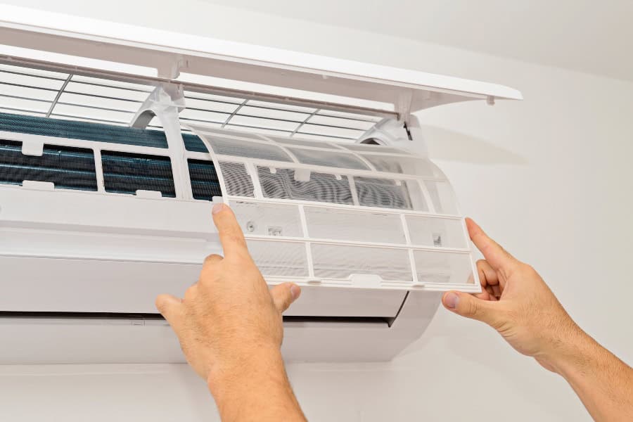 Person reinstalling clean air conditioner filters into the unit after completing AC maintenance.