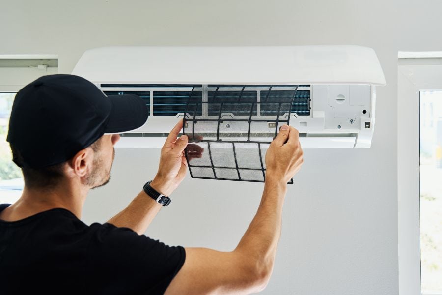 Technician removing air conditioner filter during maintenance to fix and improve performance.