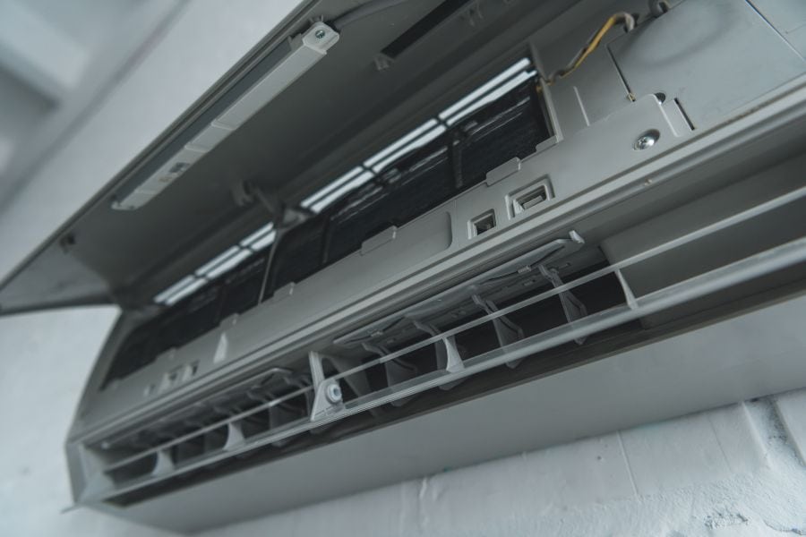 Open wall-mounted AC unit showing internal wiring, coils, and components for maintenance.