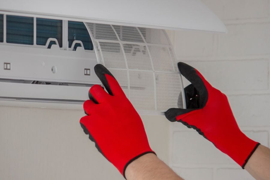 Technician wearing red safety gloves removing AC filter during routine maintenance.