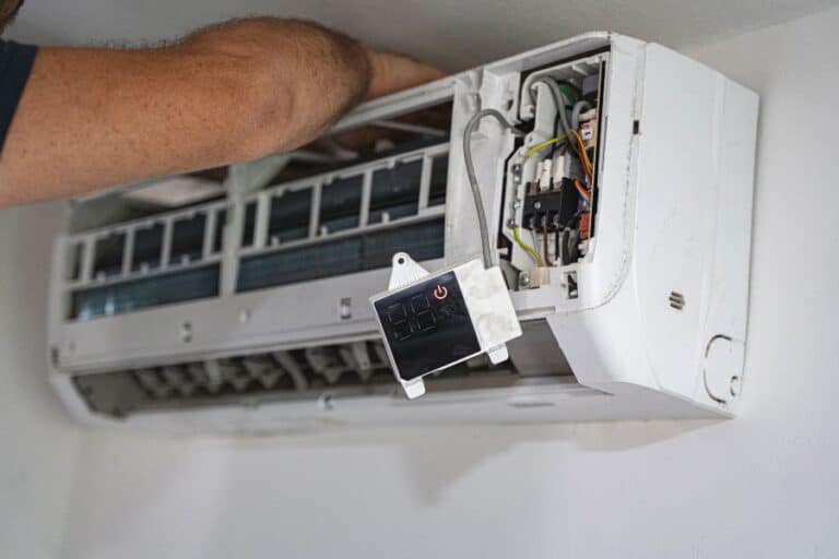 Technician repairing wall-mounted AC unit with exposed wiring and components during service.