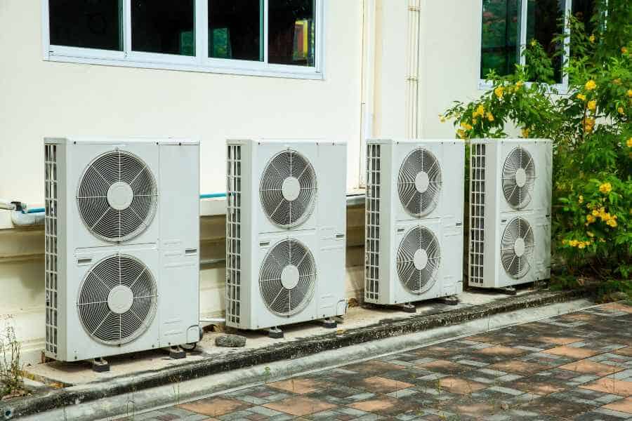 Multiple outdoor air conditioning compressor units installed beside a building wall.