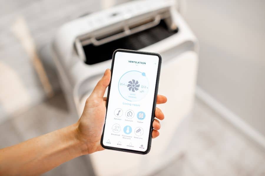 Person using a smartphone app to control a portable air conditioner for room cooling.