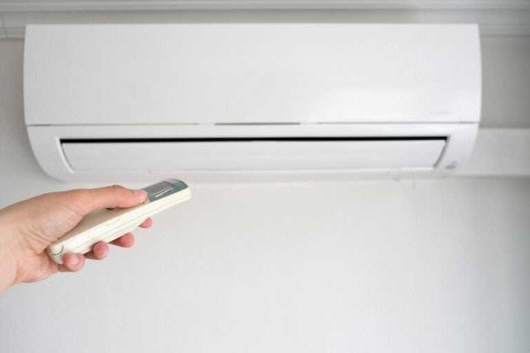 Hand holding a remote control pointed at a wall-mounted Daikin split system air conditioner.