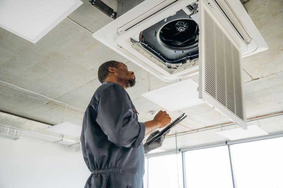Technician inspecting ducted air conditioning unit during ceiling installation.