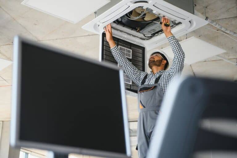 Technician servicing ducted air conditioning system in a commercial ceiling.