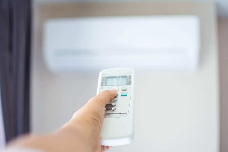 Hand using a Daikin air conditioner remote to reset settings on a wall-mounted unit.