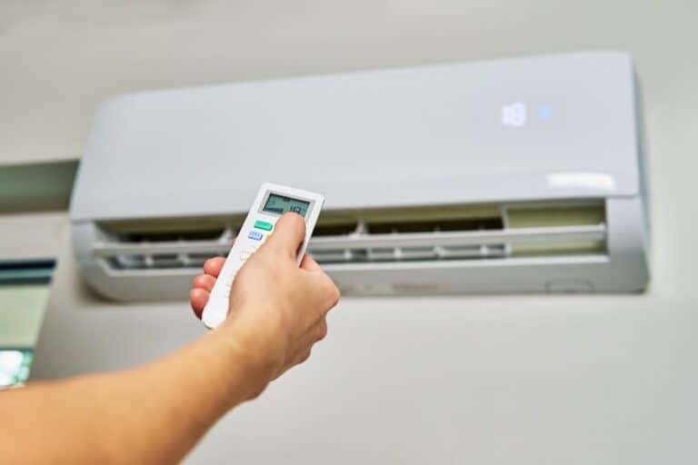 Hand holds remote adjusting digital temperature on wall-mounted air conditioner unit.