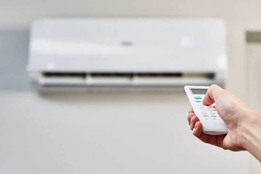 Hand using remote to adjust settings on white wall-mounted air conditioner, relating to error codes and resets.