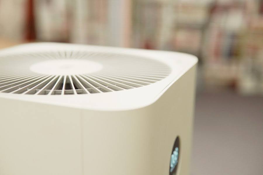 White air purifier with vented top in a soft-focus indoor setting.