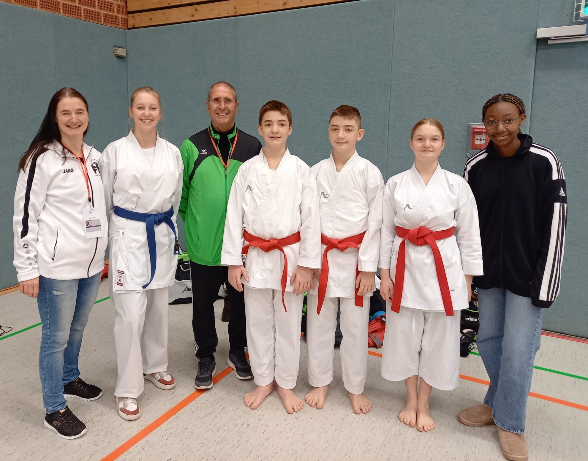 Karate-Team mit Trainer und Athleten in Sporthalle.