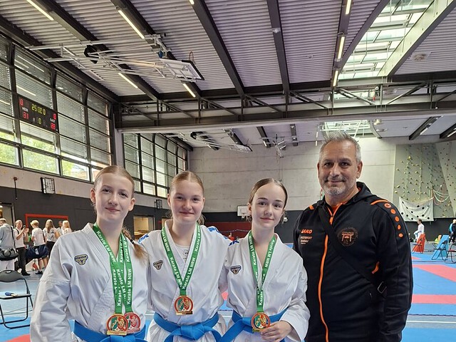 Drei Karateka mit Medaillen und Trainer in Sporthalle