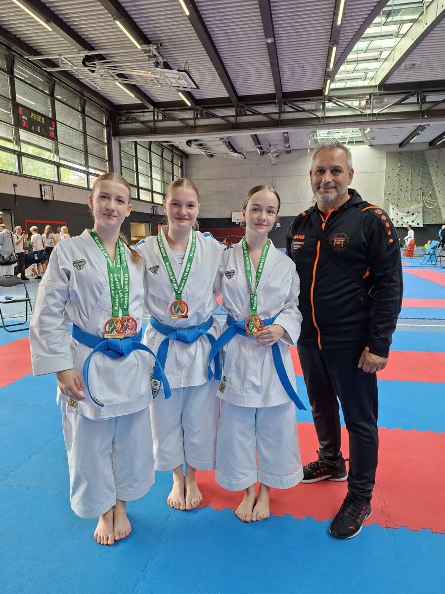 Drei Karateka mit Medaillen und Trainer in Sporthalle