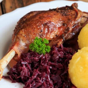 Gebratene Entenkeule mit Rotkohl und Kartoffelknödeln auf einem Teller