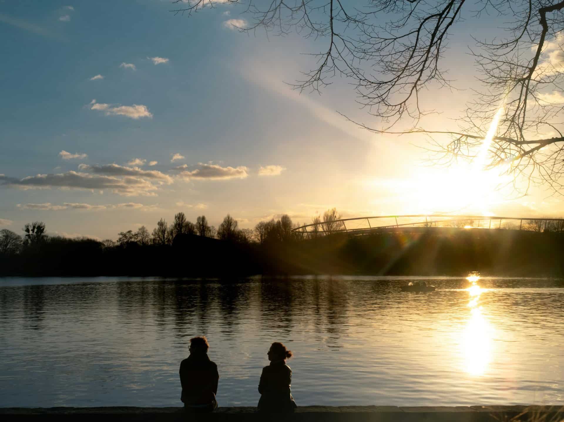 Abdenstimmung mit Blick über den Maschsee. Im Vordegrund die Silhoutte von zwei Personen am Ufer sitzend