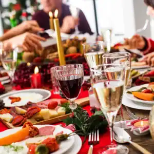 Festlich gedeckter Tisch mit Weihnachtsessen und Weingläsern. Unscharf im Hintergrund, genüsslich essende Personen.