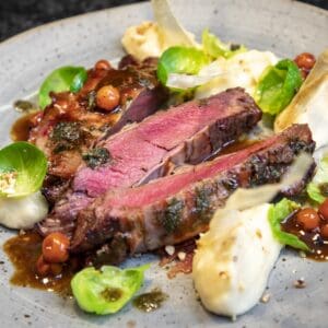 Nahaufnahme eines seltenen Hirschsteak-Filets, gewürzt mit frischen Kräutern und serviert mit Kartoffelpüree auf dem Teller