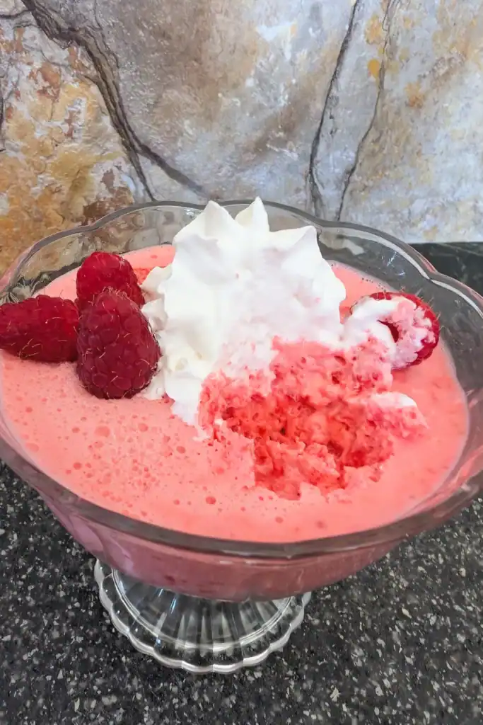 looking down on an angle at the top of the no-bake raspberry cream cheese salad in a dessert cup topped with whipped cream and berries