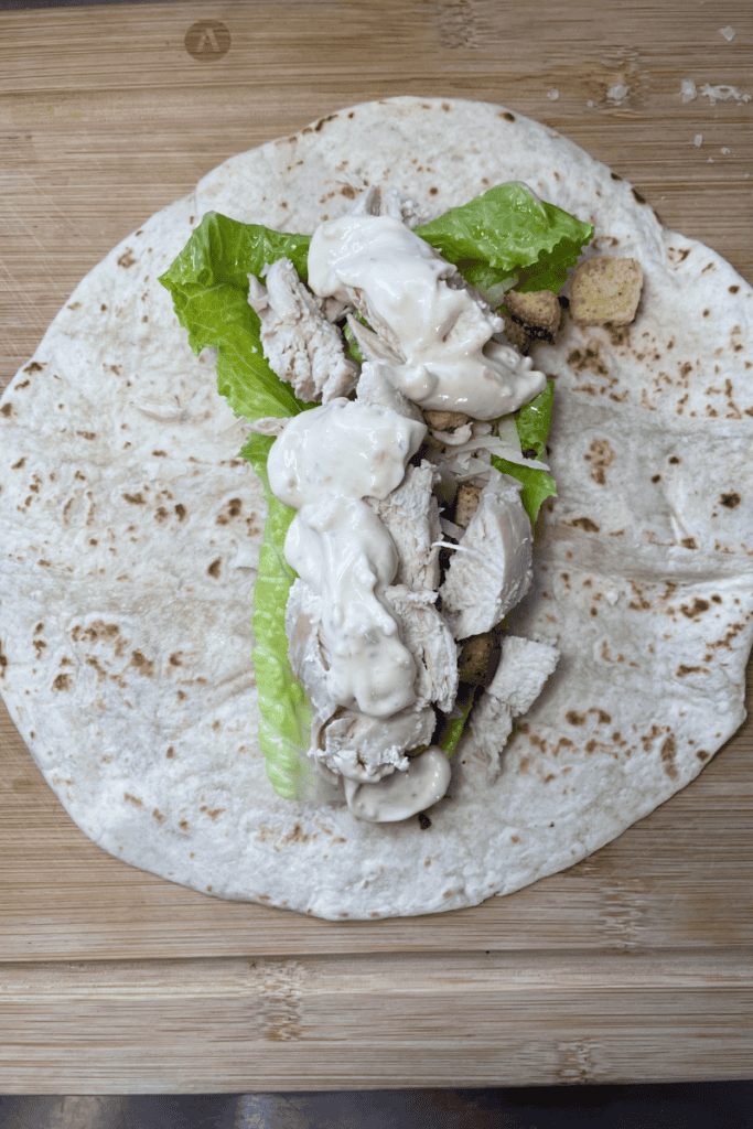 add cooked chicken breast and Caesar salad dressing to sandwich wrap