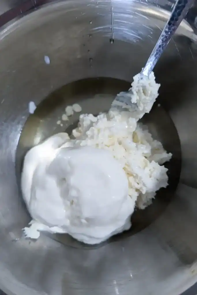 adding vanilla Greek yogurt and vegetable oil to whipped cream cheese in bowl