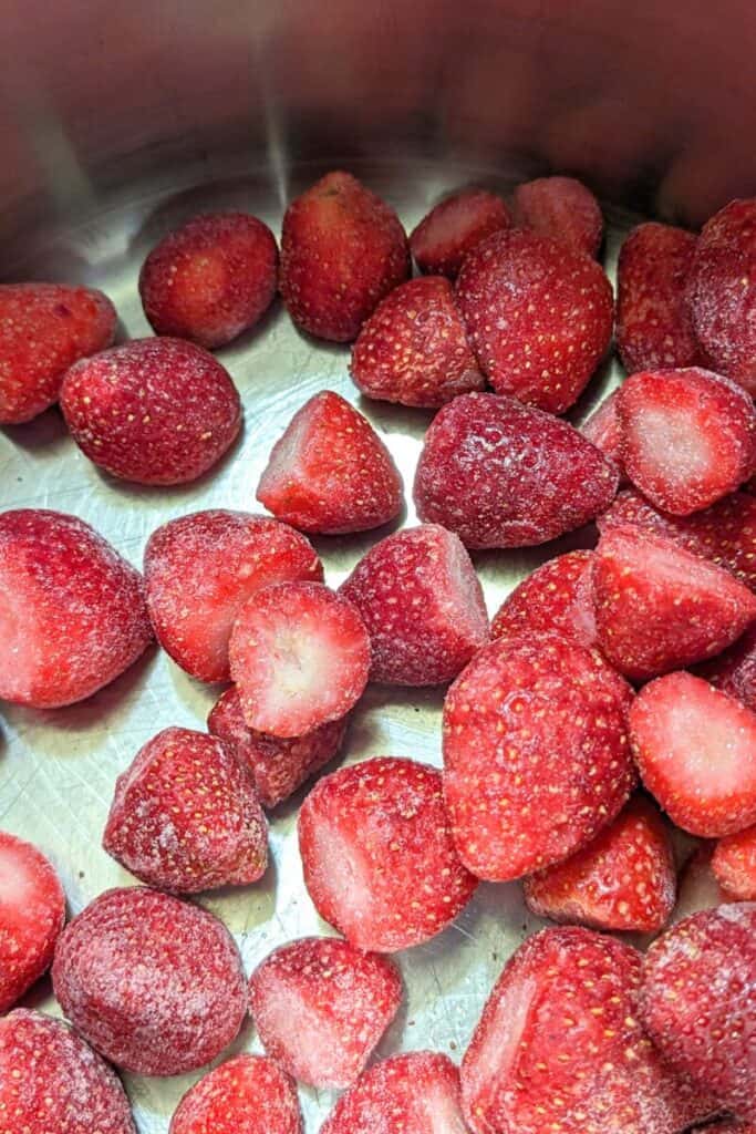 adding frozen strawberries to jam pot