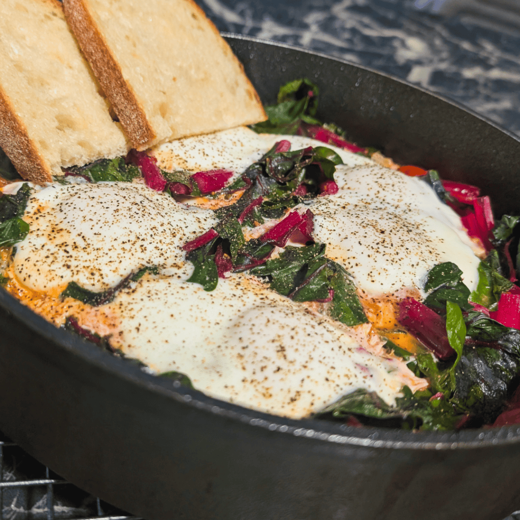 Eggs in Purgatory with toast, featuring spicy tomato sauce, greens, and perfectly cooked eggs.