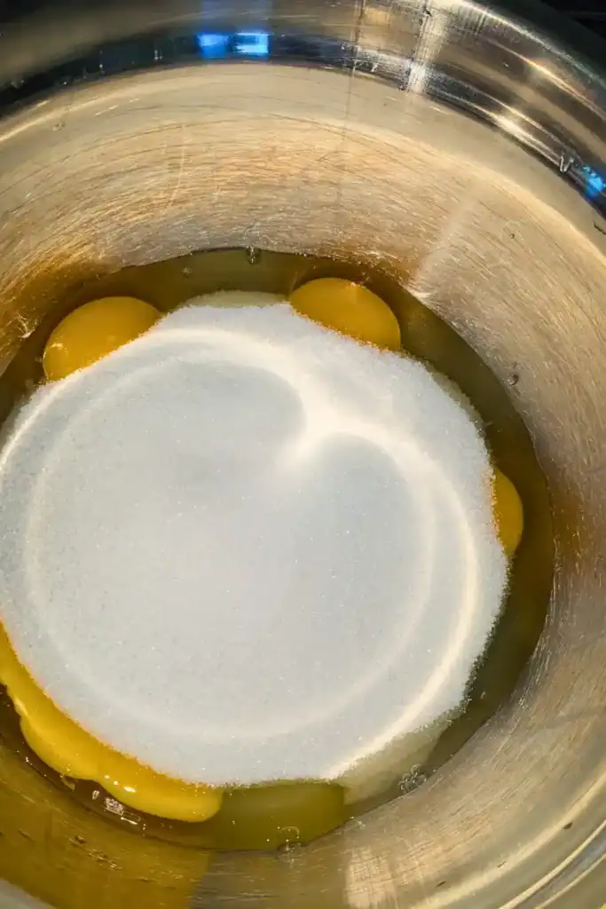 adding white sugar to eggs in mixing bowl